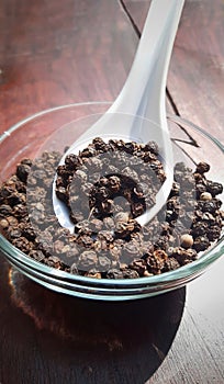 Black pepper. Black pepper or peppercorns in glass bowl with spoon in wooden background 